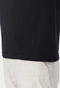 Schwarzes Baumwoll-T-Shirt mit rundem Ausschnitt und kurzen Ärmeln, sauber gesäumt und mit weicher Textur, kombiniert mit hellbeigen Leinenhosen.