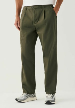 Khaki green pants with a straight fit, pleats at the front, and side pockets. Paired with gray sneakers featuring a mesh design.
