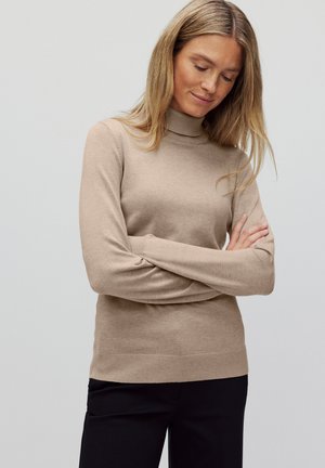 Beige polotröja i mjukt stickat material, med långa ärmar och en figursydd design, kombinerad med svarta byxor.