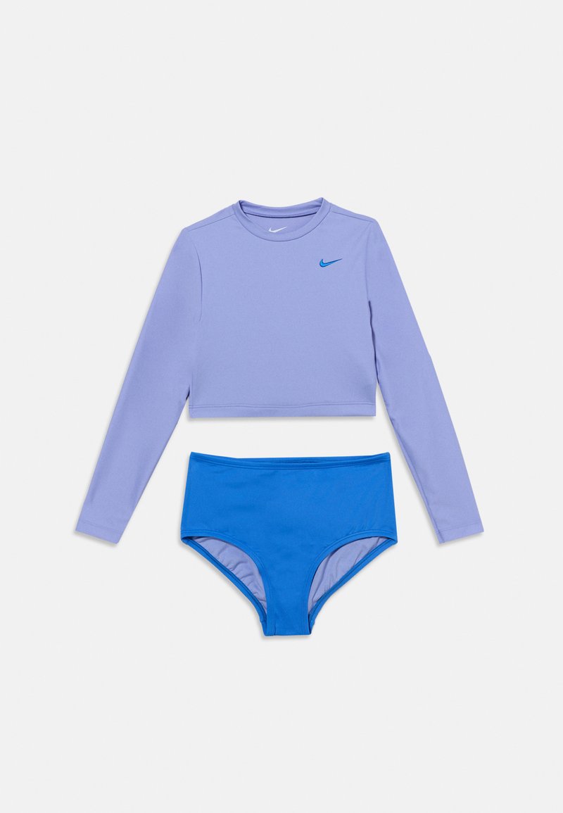 Crop top lavande à manches longues avec le logo Nike bleu, associé à un bas de maillot de bain bleu taille haute sur fond blanc.