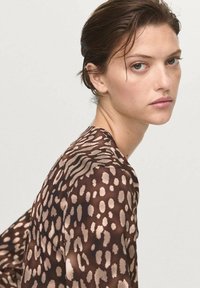 Blusa marrone a fantasia con macchie irregolari beige e righe, realizzata in un tessuto leggero e trasparente con un taglio morbido.