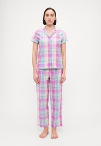 Σαλοπέτα πιτζάμα με κοντό μανίκι σε παστέλ χρώματα, με ανοιχτό ροζ, πράσινους και μωβ καρό, διαθέτει πουκαμίσα με κουμπιά και φαρδιά παντελόνια.