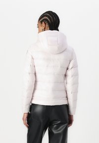Giacca puffa rosa chiaro con cappuccio, caratterizzata da cuciture orizzontali e un design elegante a trapunta. Indossata con pantaloni neri.