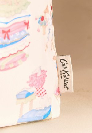 Narożnik materiału w pastelowym wzorze z metką tkaniny „Cath Kidston London” przymocowaną na beżowym tle.