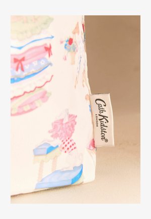 Narożnik materiału w pastelowym wzorze z metką tkaniny „Cath Kidston London” przymocowaną na beżowym tle.
