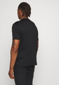 Svart t-shirt med kort ärm i avslappnad passform, tillverkad av mjukt bomullstyg med minimala sömmar, slät textur och utan synliga logotyper.