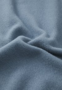 Meka plave tkanine s brušenom teksturom, koja prikazuje suptilne nabore i krivulje, što ukazuje na lagani materijal od flisa.