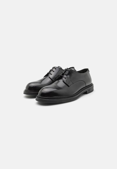 Scarpe da uomo in pelle nera con finitura liscia, punta rotonda e design con stringhe, caratterizzate da una suola a contrasto e un sottile dettaglio di branding.