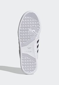 Bela podplat športnih copat z heksagonalnim vzorcem za oprijem, odtisnjenim logotipom ter tremi črnimi črtami ob strani. Gladek gumijast material.