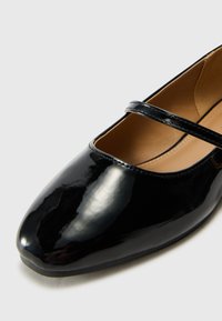 Black patent leather Mary Jane shoe with a rounded toe and a single strap across the instep. Smooth texture and subtle shine.