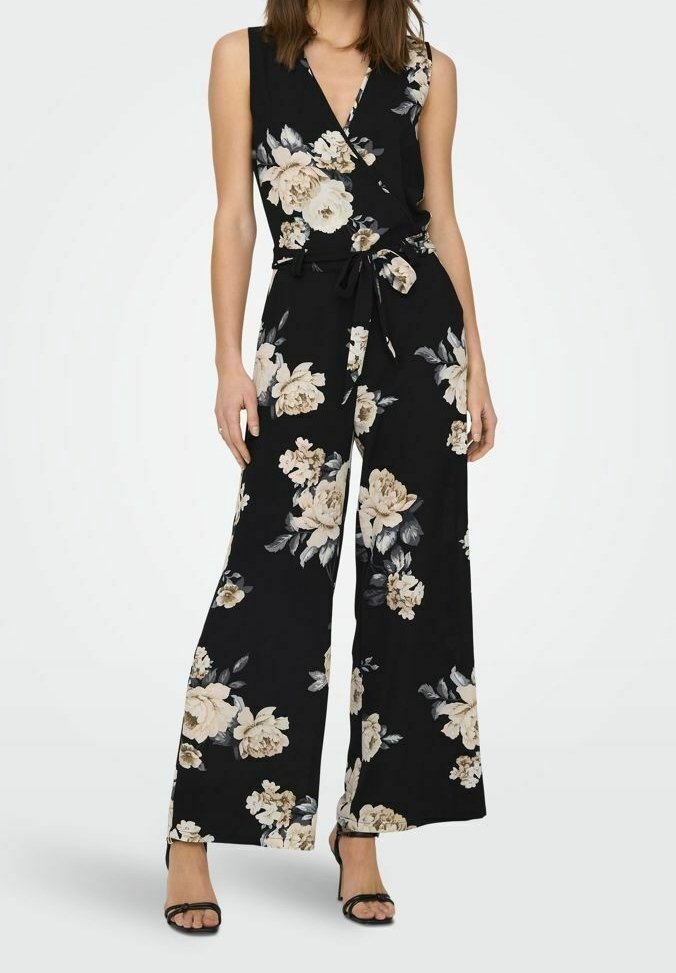 Combinaison noire sans manches avec imprimé floral beige et blanc, haut style portefeuille, jambes larges, taille nouée, et sandales noires à talons hauts.