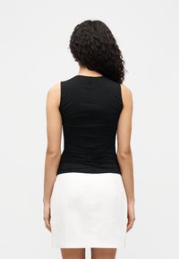 Μαύρο αμάνικο τοπ με σακουλιαστό σχέδιο στην πλάτη, συνδυασμένο με άσπρη φούστα. Λεπτή υφή και εφαρμοστό σχέδιο.