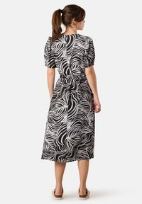Schwarz-weißes Kleid mit einem wellenförmigen Muster, puffigen Ärmeln, tailliertem Schnitt und einem knielangen Rock, gefertigt aus leichtem Stoff.