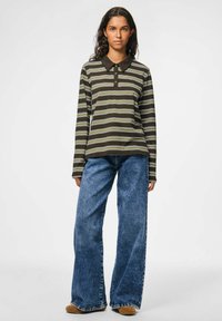 Langsleeve bruine gestreepte polo met een donkere kraag, gecombineerd met wijde blauwe jeans. Bevat knopen en heeft een losse pasvorm.