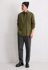 Koszula w oliwkowo-zieloną kratę, szare dopasowane spodnie i czarne sznurowane buty. Koszula ma luźny krój i podwinięte rękawy.