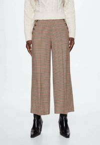 Geruite wijde broek in beige, rood en zwart; met zijknopen en een ontspannen pasvorm. De stof heeft een gladde textuur.