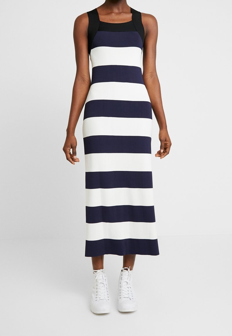 Robe maxi avec un décolleté carré, ornée de larges rayures bleu marine et blanches. Le tissu semble lisse ; associée à des baskets blanches.