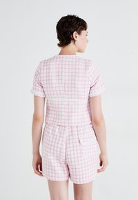 Kortermet romper i lys rosa tweed, med rutenettmønster, en tettsittende midje og en baklomme. Glatt tekstur.