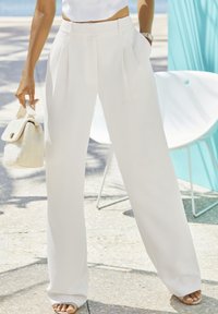 Pantaloni bianchi a gamba larga con pieghe, realizzati in un tessuto leggero. Abbinati a una borsa bianca texturizzata e sandali aperti.