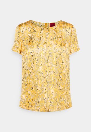 Blouse jaune à manches courtes en tissu lisse, avec un motif abstrait noir et blanc, col rond et coupe décontractée.