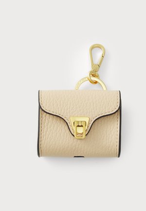 Beige leather keychain wallet with gold-tone hardware, a clasp, and a scalloped flap design. Edges have a contrasting dark trim.