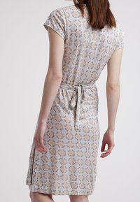 Šaty s květinovým vzorem a krátkými rukávy, vyrobené z měkké tkaniny. V pase se zavazují a mají délku po kolena s bočními rozparky.