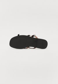 Semelle noire avec une surface lisse et plate ; présente deux sangles marron avec des accents métalliques pour la fermeture ; design et forme minimalistes.