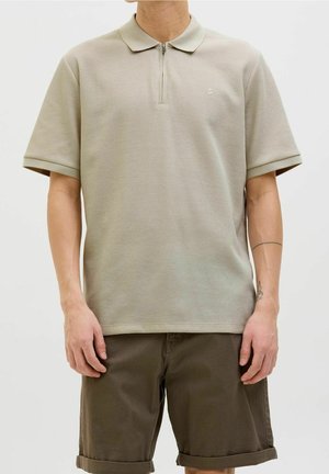Polo triko s krátkým rukávem v světle béžové barvě, vyrobené z texturované tkaniny. Obsahuje zipový límec a malé logo na hrudi. Spárováno s hnědými šortkami.