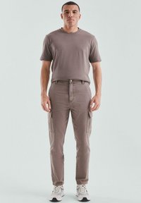 Bruine katoenen cargobroek met zijzakken, gecombineerd met een bijpassend T-shirt met korte mouwen, aangevuld met lichtgekleurde sneakers.