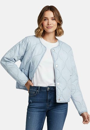 Lichtblauwe doorgestikte jas met golfpatroon, drukknopen en zijzakken, gecombineerd met een wit overhemd en donkere spijkerbroek.