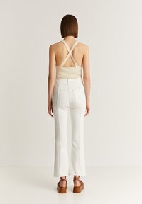 Un débardeur beige à dos croisé associé à un jean blanc évasé. La tenue présente un design minimaliste avec des textures douces et des chaussures à plateforme marron.