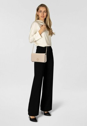 Borsa a tracolla beige con catena dorata, design rettangolare elegante e dettaglio logo, abbinata a pantaloni neri a gamba larga e una camicetta crema.