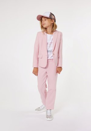 Lichtroest pak met een blazer met één knoop, gecombineerd met een witte graphic t-shirt en zilveren sneakers. Afgemaakt met een witte pet met een gaasachterkant.