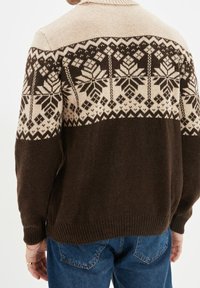 Maglione lavorato a maglia con un design a blocchi di colore beige e marrone scuro, caratterizzato da un motivo a fiocco di neve nella parte superiore e orlo a coste.