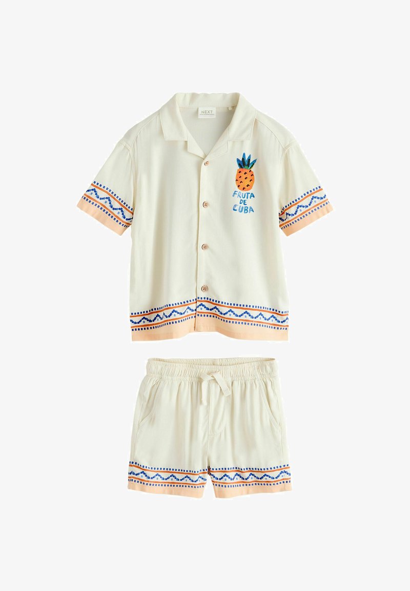 Ensemble composé d'une chemise crème à manches courtes avec boutons et d'un short, orné d'un liseré géométrique bleu et pêche ainsi que d'un motif d'ananas avec l'inscription « Fruta de Cuba ».