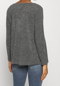 Šedý texturovaný top s dlouhým rukávem a širokým výstřihem, volného střihu, v kombinaci s modrými dobře padnoucími džíny. Zadní strana má švy.