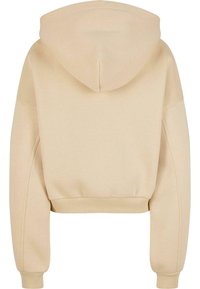 Skrajen béžový mikina s mäkkou textúrou, ktorá má kapucňu, rebrovaný lem a spadnuté plecia pre uvoľnený strih.
