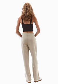 Beżowe spodnie szerokie z mi�ękkiego materiału, z gładkim paskiem w talii. Modelka ma na sobie czarny prążkowany crop top i białe buty.