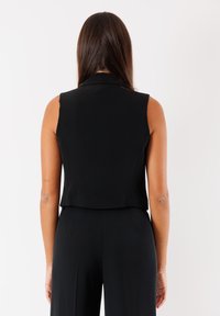 Gilet nero senza maniche con un design strutturato, caratterizzato da una lunghezza leggermente accorciata, una texture liscia e senza chiusure visibili.
