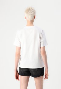 Hvit bomulls T-skjorte med rund hals, korte ermer og løs passform, kombinert med mørke denimshorts, sett fra ryggen.