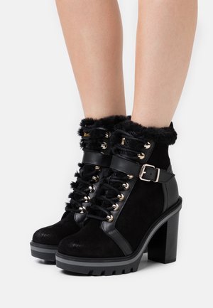 Bottines noires avec garniture en fausse fourrure, dessus en daim, œillets de lacet métalliques et talon bloc. Présente des accents de boucle et une semelle texturée.