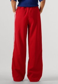 Rode wijdlijnbroeken van gladde stof, met witte zijkanten en twee achterzakken. De tailleband is elastisch voor extra comfort.