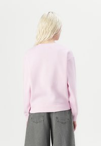 Felpa rosa chiaro con colletto rotondo e maniche lunghe, caratterizzata da orli e polsini a coste, indossata con pantaloni ampi grigi.