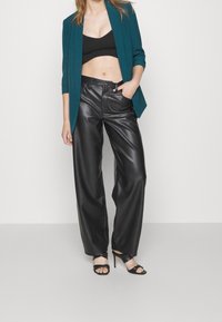 Turkusowa marynarka na czarnym topie na krótko, zestawiona z czarnymi skórzanymi spodniami z wysokim stanem i czarnymi sandałami na obcasie. Gładka faktura, dopasowany krój.