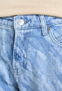 Jeans de denim azul claro com uma textura desgastada, apresentando um fecho com botão prateado e costuras em destaque, realçando um padrão de lavagem desbotado.