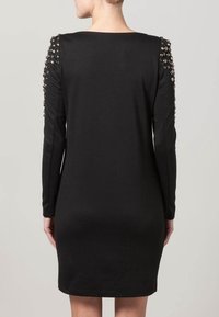 Robe noire à manches longues avec des accents d'épaule ornés de clous métalliques. Design ajusté, longueur genou, texture de tissu lisse.