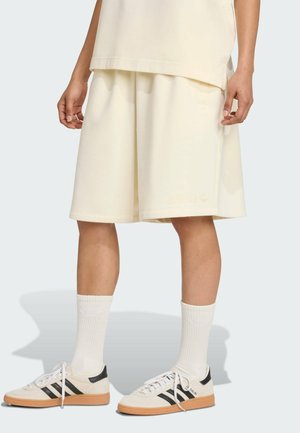 Crème-kleurige sportshorts met subtiele branding, gecombineerd met witte geribde sokken en zwart-witte sneakers met een gumsole.