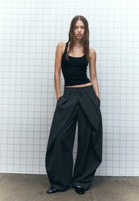 Zwarte tanktop gecombineerd met brede, donkergrijze pantalon met streepjespatroon, featuring een unieke gedrapeerde design en twee zijzakken.