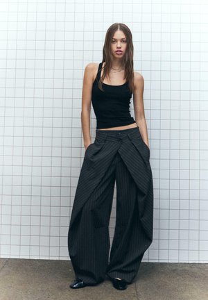 Top nero abbinato a pantaloni larghi a righe grigie scure con un design drappeggiato unico e due tasche frontali.