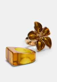 Zwei Ringe: einer aus rechteckigem, bernsteinfarbenem, durchscheinendem Harz; der andere im floralen Design mit goldfarbenen Akzenten und bernsteinfarbenen Blütenblättern.